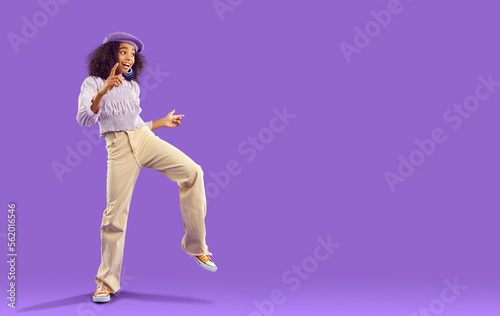 Overjoyed teen african american girl in funky cool clothes dance isolated on purple studio background. Funny biracial teenager have fun make dancer moves. Youth hobby and entertainment. Copy space.