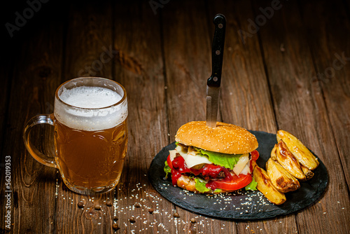 From above view of homemade beef burger with mug of beer, baked potato, on wood table 