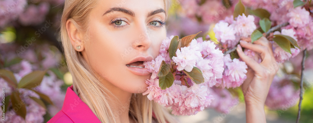 Fototapeta premium Sensual woman near sakura tree background, banner for website header. Spring girl fashion. The tongue. Blossom woman.