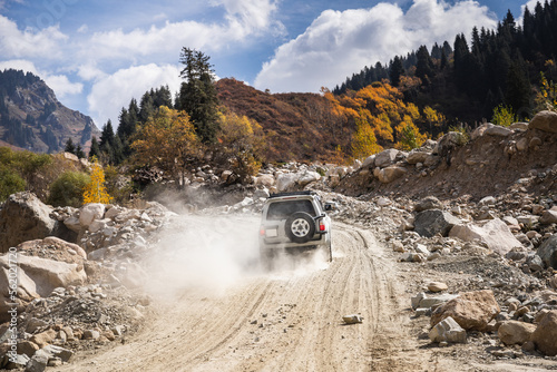 White SUV car climbs a dusty road in the autumn mountains.