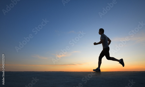 Fototapeta Naklejka Na Ścianę i Meble -  Silhouette view of a man jogging on road with dawn sky background.