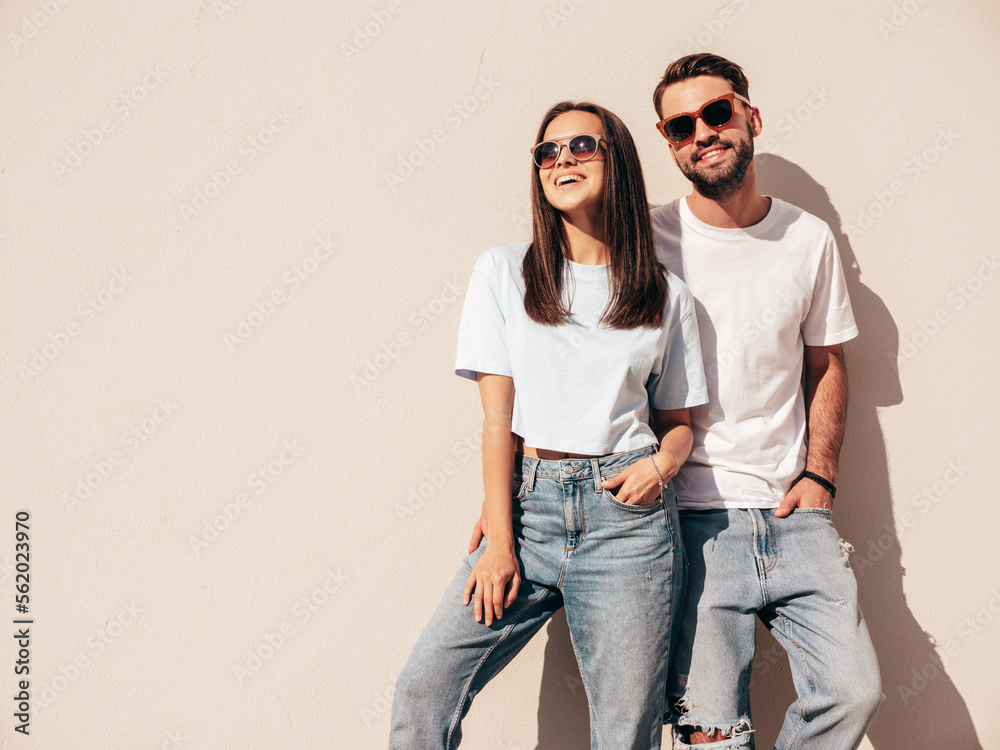 Smiling beautiful woman and her handsome boyfriend. Woman in casual summer jeans clothes. Happy cheerful family. Female having fun. Sexy couple posing in the street at sunny day. Near white wall - obrazy, fototapety, plakaty 