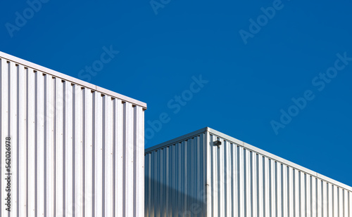 Two corrugated metal industrial warehouse buildings against blue clear sky background in perspective side view