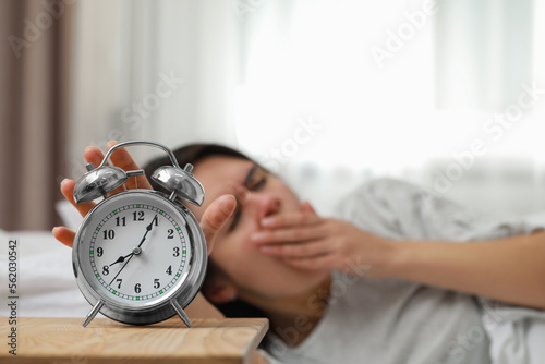 Yawning woman turning off alarm clock in bedroom, focus on hand. Space for text