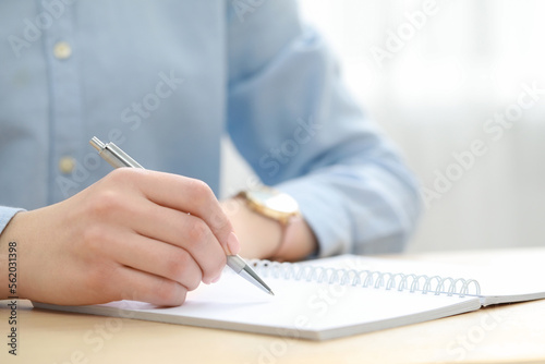 Woman writing in notebook at wooden table, closeup