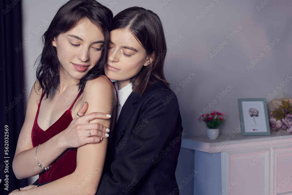 Close-up shot of a two lesbian girls looks at an engagement ring, cuddling and enjoying an intimate moment at home. One girl wearing a black suit, another girl wearing a red dress. LGBT concept.