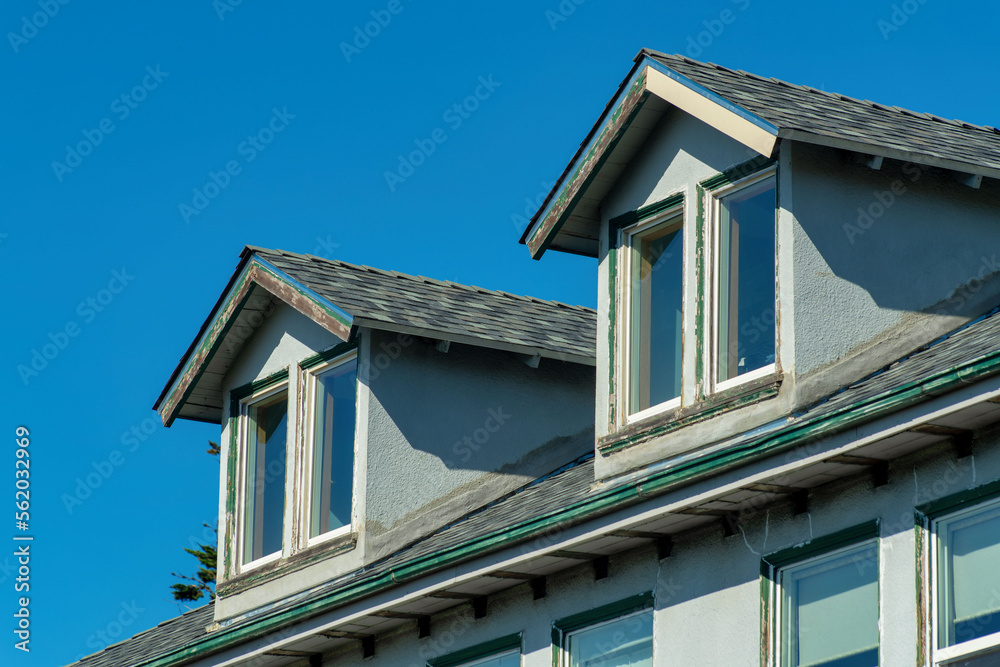 Double tiny roofs on window skylights with dark roof tiles and blue stucco facade exterior with clear sky background