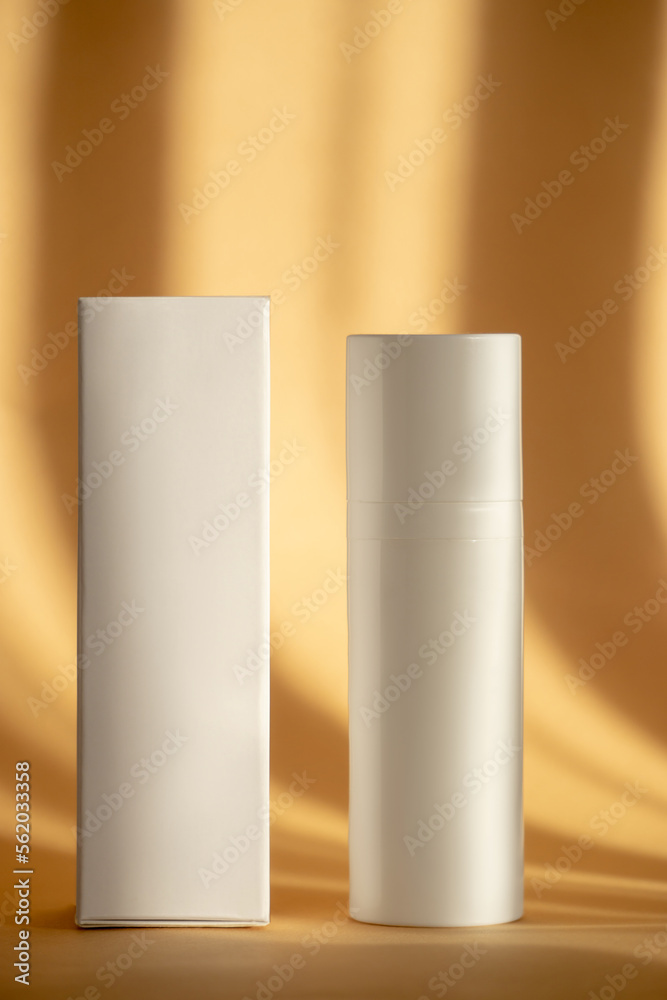 Face lotion in white unmarked bottle and packing box on brown background. Blank container for shampoo, foam, gel for washing in sunlight. Mockup style. Vertical image Face lotion in white unmarked bottle and packing box on brown background. Blank container for shampoo, foam, gel for washing in sunlight. Mockup style. Vertical image