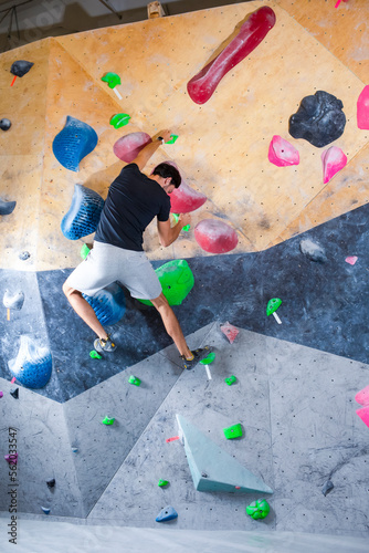 One Rock climber man hanging on a bouldering climbing wall, inside on colored hooks.