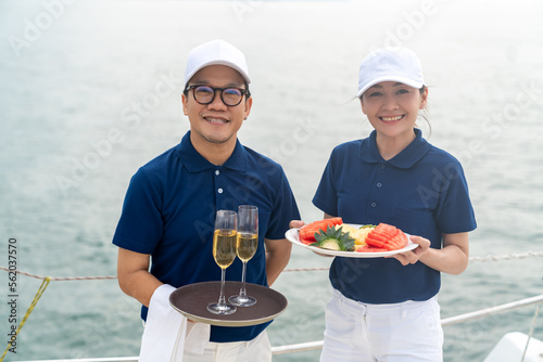 Portrait of Waiter and waitress holding fresh fruit and champagne for serving to passenger tourist travel on luxury catamaran boat yacht on summer vacation. Cruise ship service occupation concept. © CandyRetriever 