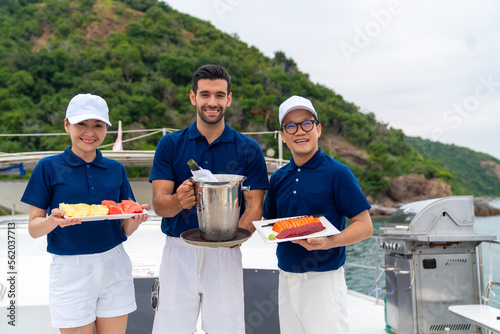 Portrait of Waiter and waitress holding food and drink for serving to passenger tourist travel on luxury private catamaran boat yacht on summer vacation. Cruise ship service occupation concept.