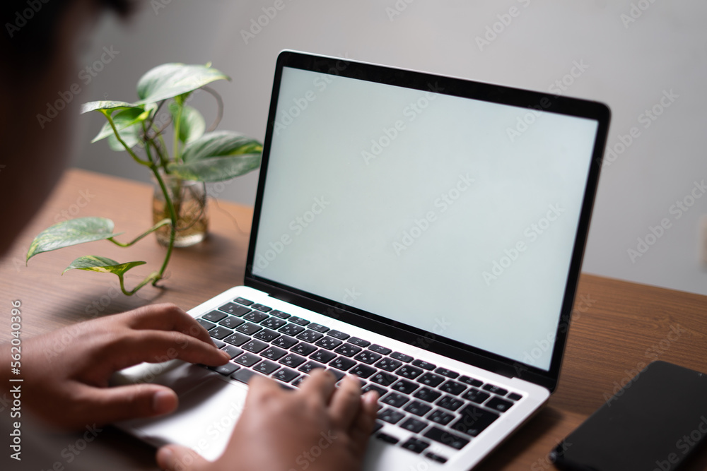 Fototapeta premium Man typing on a laptop with a white blank screen for mockup