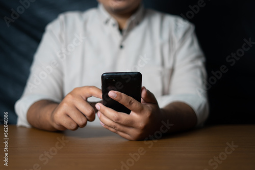 business man holding a smartphone and scrolling on a wooden table © berkahjayamaterial