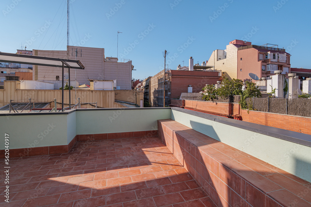 Fototapeta premium Big sunny terrace on the roof of modern building lined with red brick tiles overlooking the neighboring houses. Summer playground for leisure activities, party and meetings with friends.