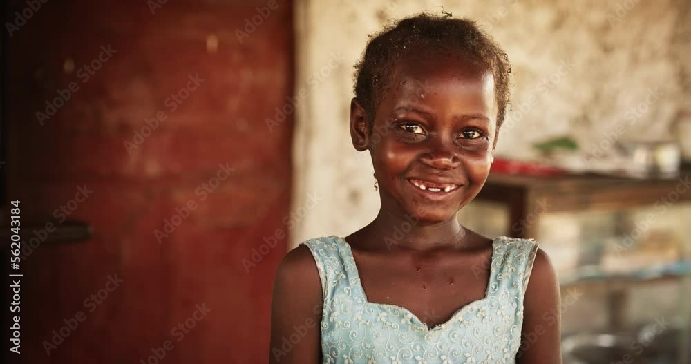Close Up Portrait of a Shy Authentic African Little Girl Smiling at the Camera with Blurred Background. Black Female Kid Representing Future, Hope, and Acceptance. Documentary Concept