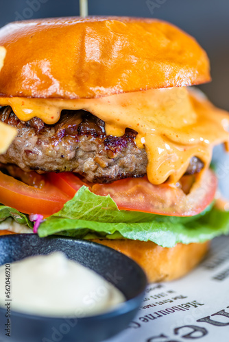 A hamburger with cheese, lettuce and tomato and a bowl of aioli sauce