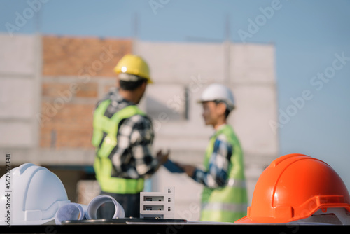 Orange and white hard hat on workbench, construction engineer talking to architect at construction site or building site starting planning new project contract.