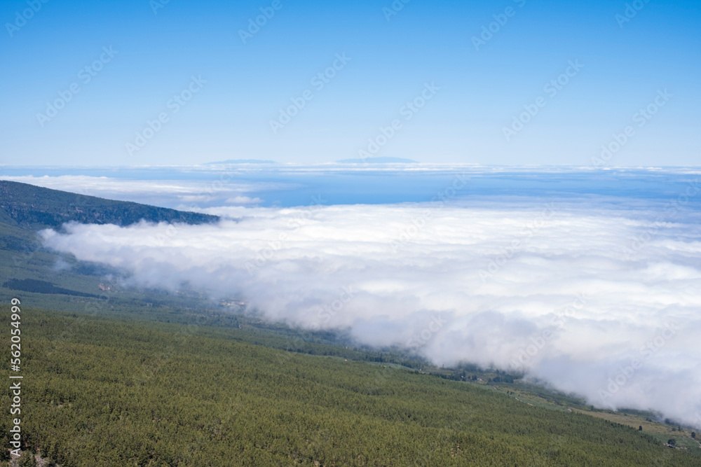 Horizontal landscape of sea of clouds, slopes of a mountain, national park of Las cañadas del Teide. Banked clouds, cloudy sky. Volcano, lava, red earth, vegetation. Tenerife, canary islands, spain.