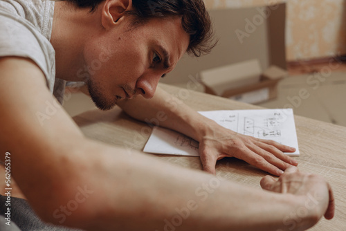 Concentrated man with furniture assembly instruction assembling wooden table at home 