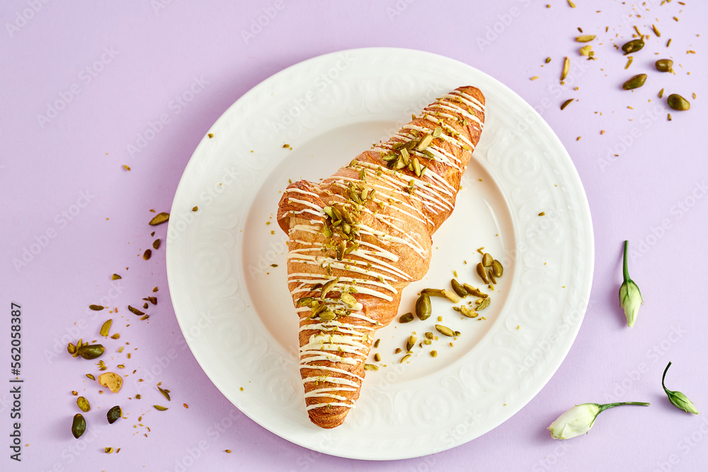 Croissant with pistachio cream and sprinkle of nuts on a white plate on a pink background Croissant with pistachio cream and sprinkle of nuts on a white plate on a pink background