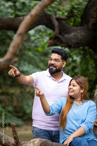 Young indian couple pointing and watching opposite site at park.