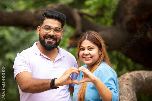 Young indian couple making heart shape with hand at park.