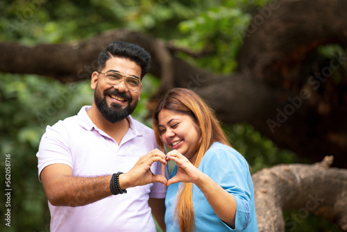 Young indian couple making heart shape with hand at park. © Niks Ads