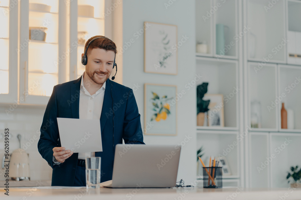 Smiling manager holding paper while typing on laptop Smiling manager holding paper while typing on laptop