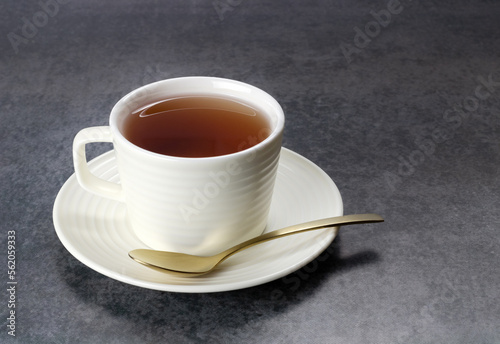 A cup of tea in a white ceramic mug and a spoon on a gray background.