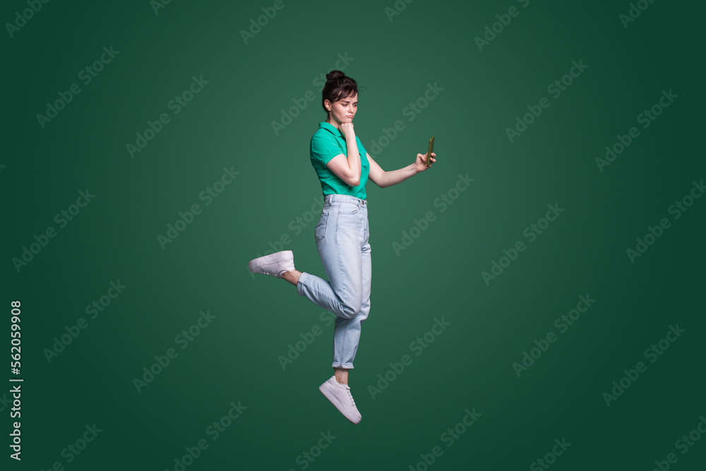 Full length portrait of a thoughtful doubtful woman talking on mobile phone isolated over green background.