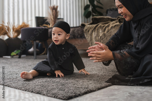 Happy Muslim family, Muslim boy sits on floor and looking at some one and his mother taking care of him nearby, Muslim woman in black hijab