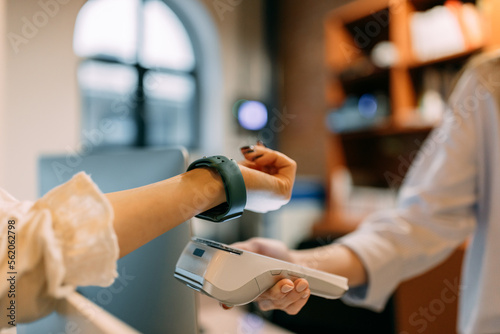 Female worker holding a paying machine, customer paying with a smart watch. photo