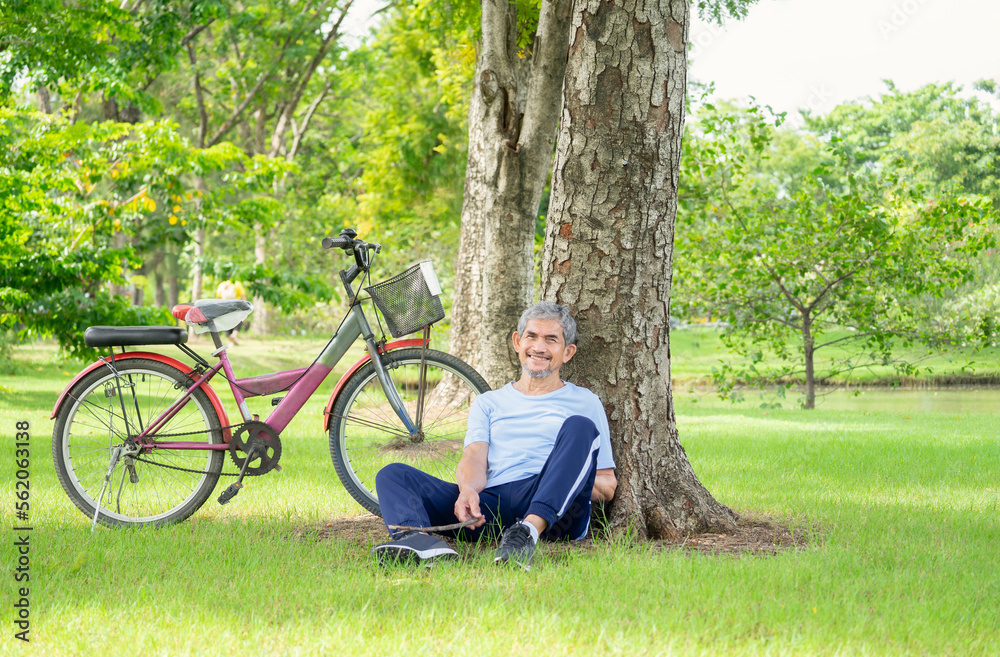 happy senior man sitting under a tree with a bicycle parked beside him, concept elderly people lifestyle, exercise, relaxing,resting happy senior man sitting under a tree with a bicycle parked beside him, concept elderly people lifestyle, exercise, relaxing,resting