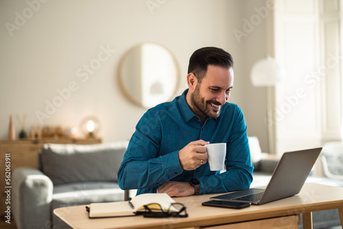A smiling man having an online meeting, holding a cup of coffee, sitting at the office.