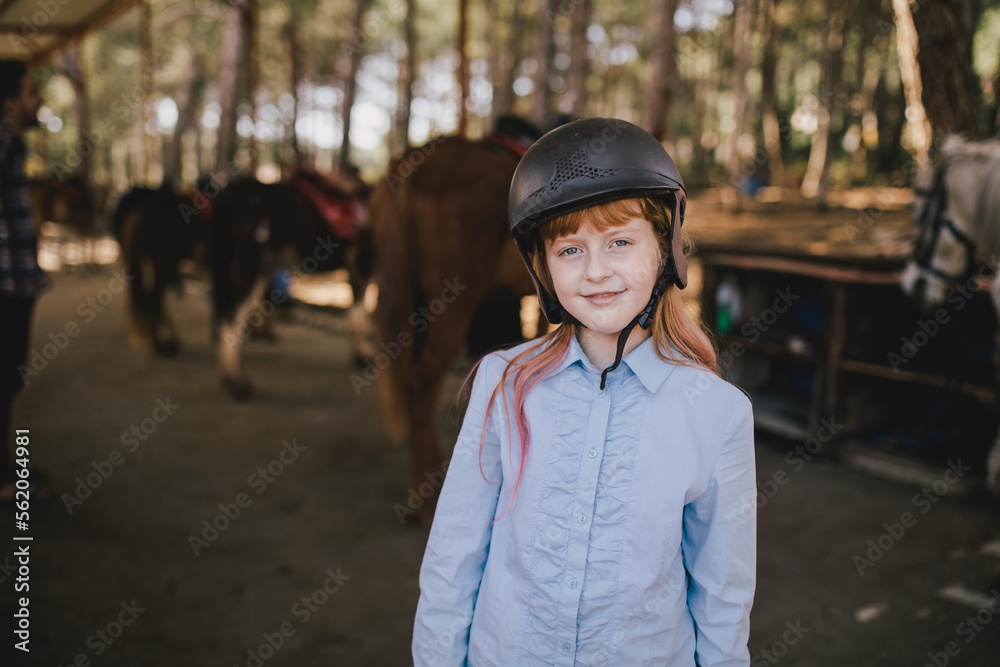 Young girl posing in a stable with the horses on the background.