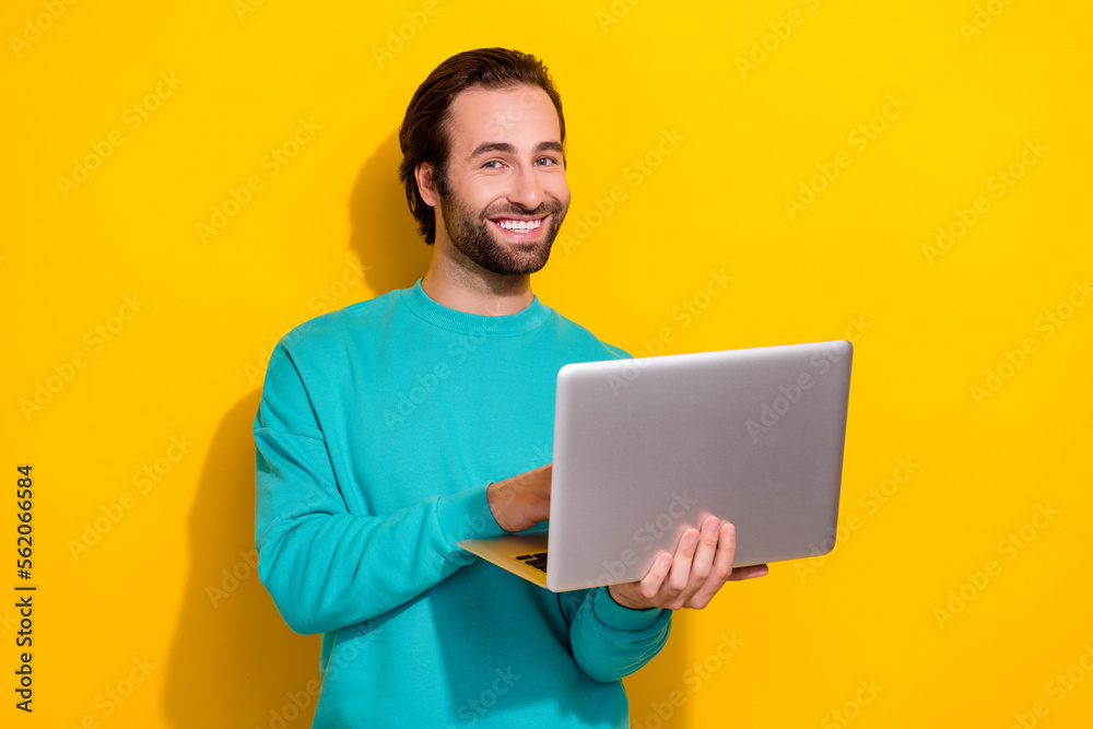 Photo of cheerful good mood smiling it coder professional programmer hold his samsung laptop app developer isolated on yellow color background Photo of cheerful good mood smiling it coder professional programmer hold his samsung laptop app developer isolated on yellow color background
