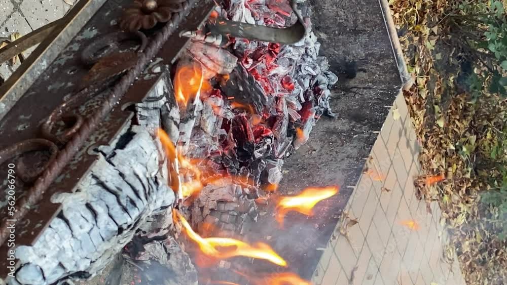Unrecognizable person prodding stirring open fire with metal poker outdoors. Preparation coals for barbecue grill. Firewood burning on grill. BBQ equipment. Picnic. Vertical shot Unrecognizable person prodding stirring open fire with metal poker outdoors. Preparation coals for barbecue grill. Firewood burning on grill. BBQ equipment. Picnic. Vertical shot