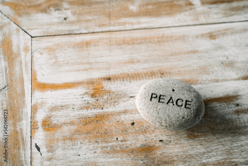 A grey stone with the inscription peace lying on a wooden table.