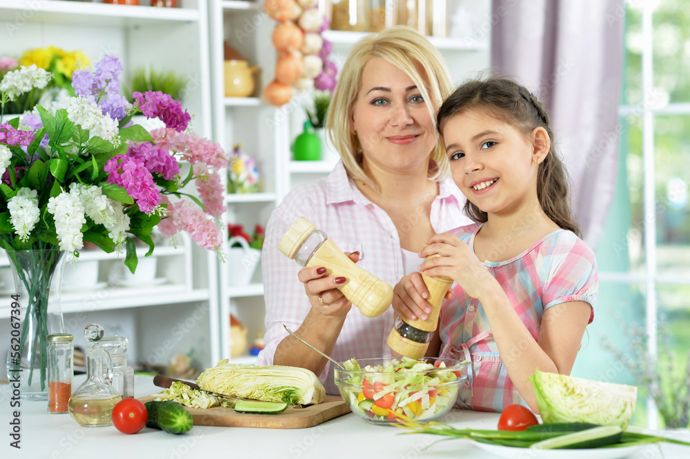 Cute little girl with her mother cooking together at kitchen table