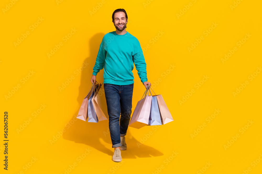 Full length photo of good mood cute guy dressed teal outfit holding bargains empty space isolated yellow color background Full length photo of good mood cute guy dressed teal outfit holding bargains empty space isolated yellow color background