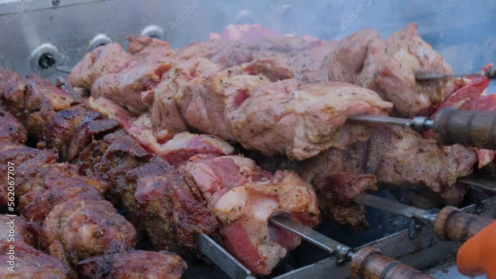 Shish Kebab on Skewers is Cooked on the Grill at Street Food Festival. Close-up. Automatic grill turns skewers. Prepares meat on coals. Street kitchen. Fresh grilled food. Shish Kebab on Skewers is Cooked on the Grill at Street Food Festival. Close-up. Automatic grill turns skewers. Prepares meat on coals. Street kitchen. Fresh grilled food.