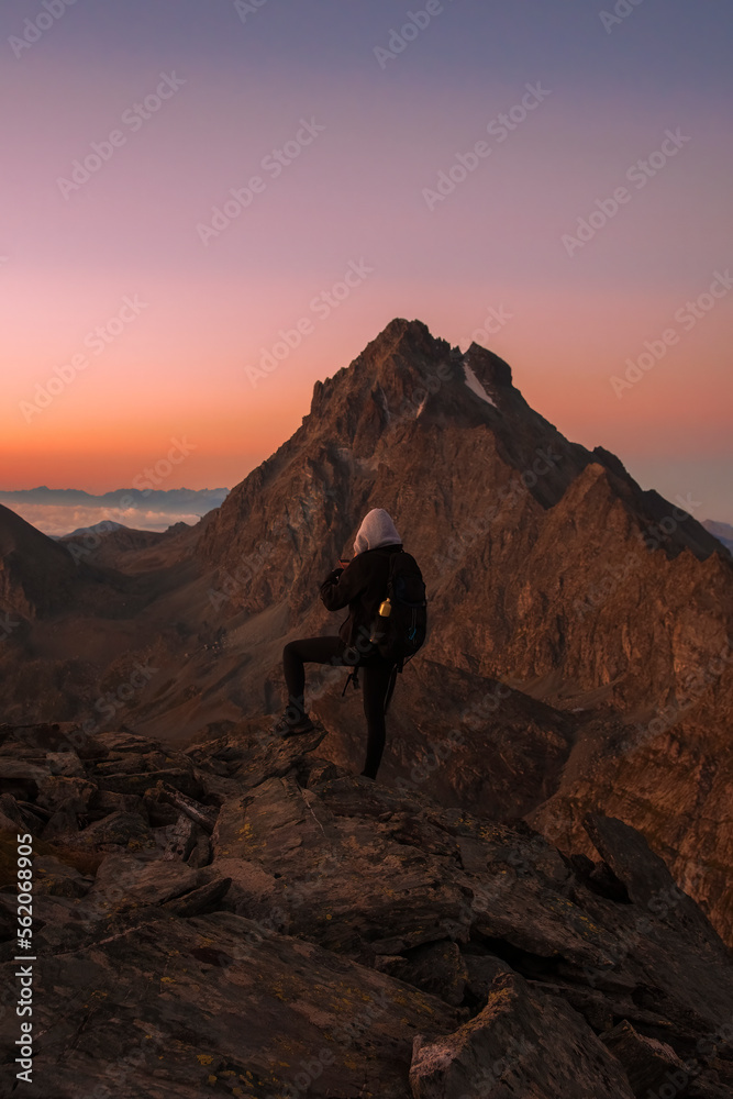 A hiker taking photos of an amazing high altitude sunrise from a mountain top as clouds enshroud the valley below. Mountain tourism concept. Italian Alps, Monviso (2841 m)