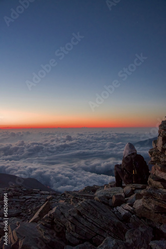 Obraz na płótnie A hiker taking photos of an amazing high altitude sunrise from a mountain top as clouds enshroud the valley below. Mountain tourism concept. Italian Alps, Monviso (3841 m) w salonie