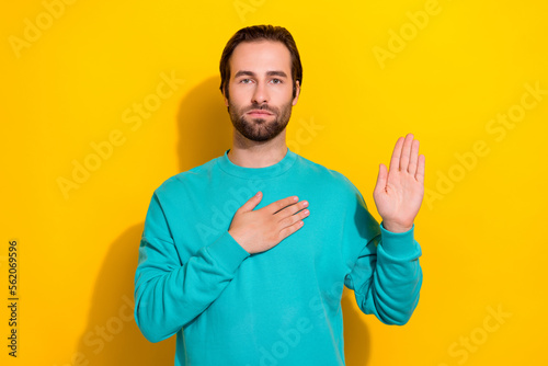Photo of honest oath brunet hair young serious man touch chest palm showing trust respect confident person isolated on yellow color background photo