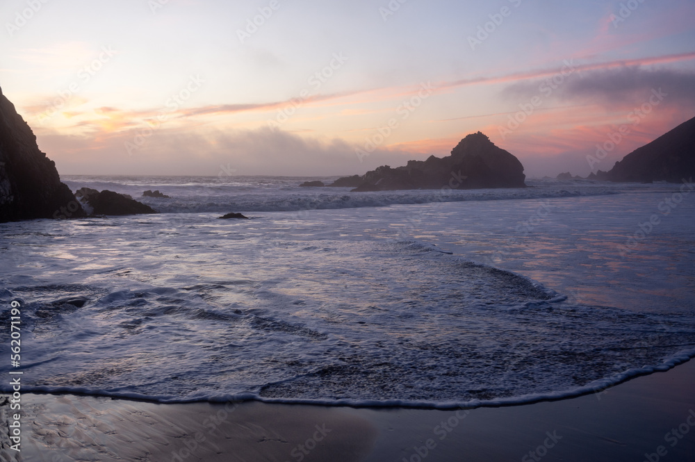 Tidal waves flowing out at Pfeiffer beach, while it is enshrouded by a purble sunset color.