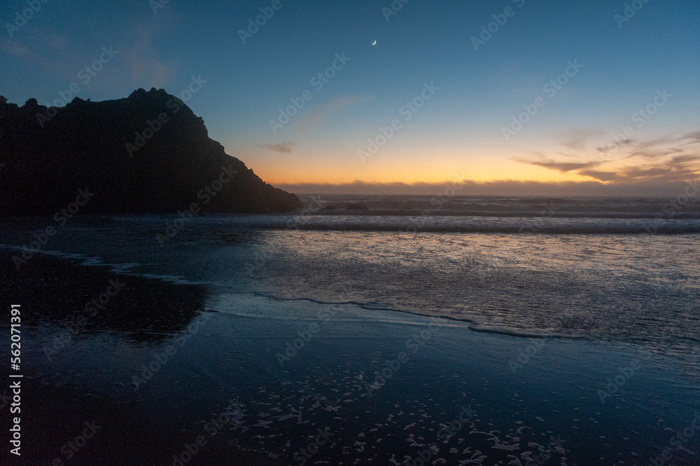 A crescent moon illuminates the beach, just after sunset, at Pfeiffer Beach. Big Sur, California. A crescent moon illuminates the beach, just after sunset, at Pfeiffer Beach. Big Sur, California.