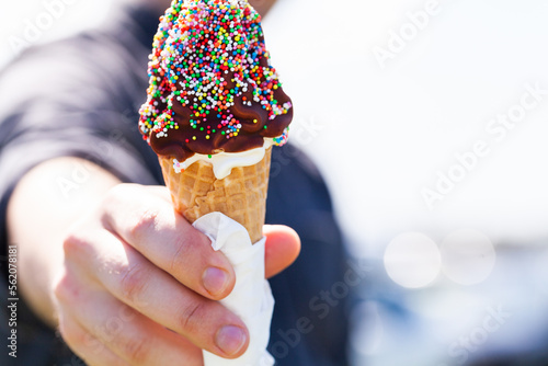 Person holding out soft serve ice-cream in waffle cone with chocolate and sprinkles photo