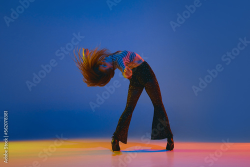 Portrait of young, dancer, girl dancing heels dance in stylish clothes over blue background in neon light. Concept of modern dance style