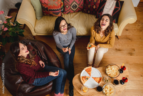 From above company of cheerful ethnic female friends eating pizza while gathering at home at weekend photo