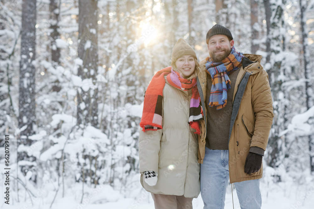 Portrait of young happy couple smiling at camera while spending their weekends outdoors in winter forest